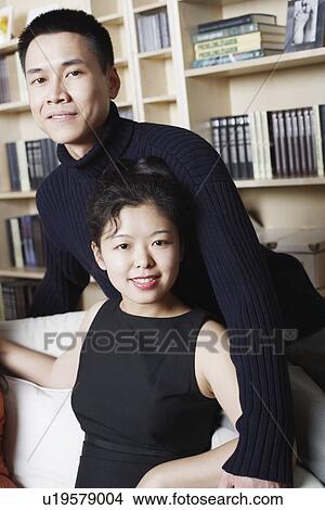 Picture - Portrait of a young woman sitting on a couch with a young man standing behind her. Fotosearch