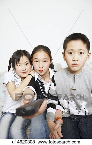 Stock Photo - Portrait of a young woman sitting with her sister and her brother holding a remote control. Fotosearch