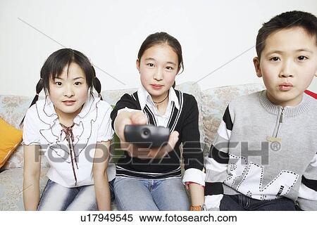 Stock Photography - Portrait of a young woman sitting with her sister and her brother holding a remote control. Fotosearch