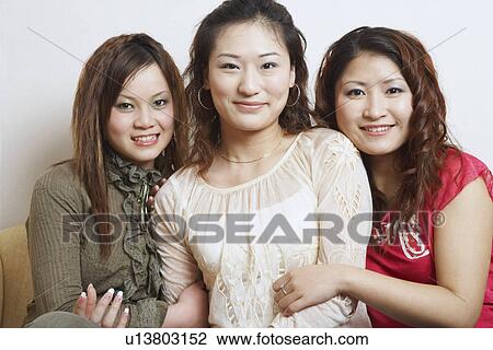 Stock Image - Portrait of three young women sitting together smiling. Fotosearch