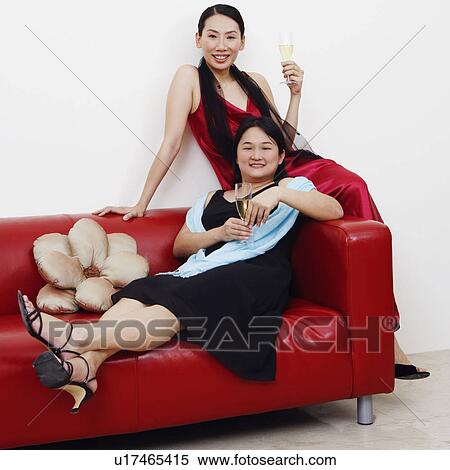 Stock Photography - Portrait of two mid adult women sitting on a couch with champagne flutes and smiling. Fotosearch