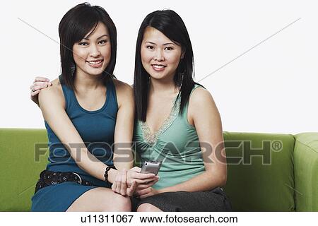 Stock Photo - Portrait of two young women holding a mobile phone. Fotosearch