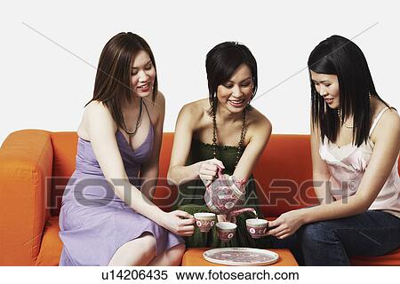 Three young women sitting on a couch with tea cups View Large Photo Image Stock Photography - Three young women sitting on a couch with tea cups. Fotosearch