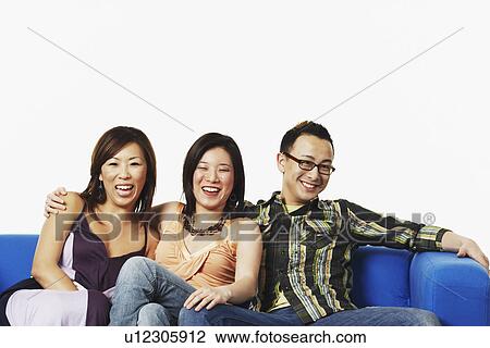 Stock Image - Two young women and a young man sitting on a couch. Fotosearch