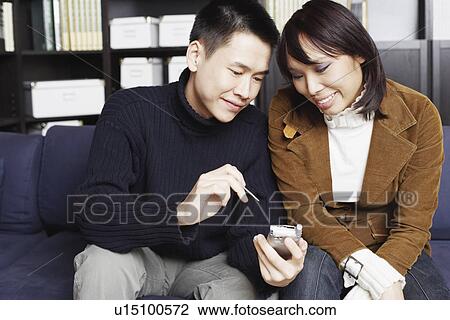 Young man sitting on a couch with a young woman holding a mobile phone View Large Photo Image Stock Image - Young man sitting on a couch with a young woman holding a mobile phone. Fotosearch