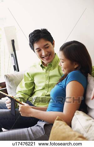 Close-up of a young couple looking at a picture frame and smiling on a couch View Large Photo Image Stock Image - Close-up of a young couple looking at a picture frame and smiling on a couch. Fotosearch