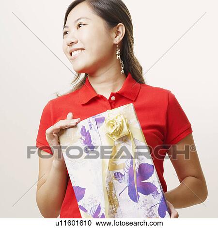 Stock Image - Close-up of a young woman holding a gift and smiling. Fotosearch