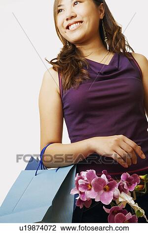 Stock Image - Low angle view of a young woman carrying flowers in a shopping bag. Fotosearch