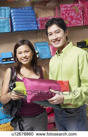 Stock Image - Portrait of a young couple holding pillows in a store and smiling. Fotosearch