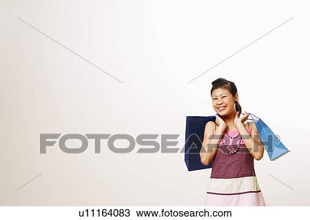 Stock Image - Portrait of a young woman carrying shopping bags and smiling. Fotosearch