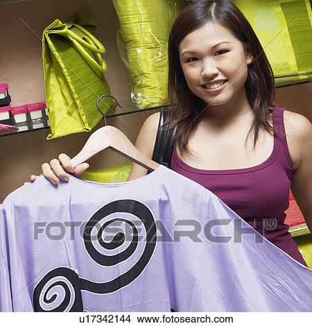 Portrait of a young woman choosing a dress in a store and smiling View Large Photo Image Picture - Portrait of a young woman choosing a dress in a store and smiling. Fotosearch