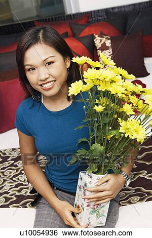 Stock Photograph - Portrait of a young woman holding a flower vase and smiling. Fotosearch