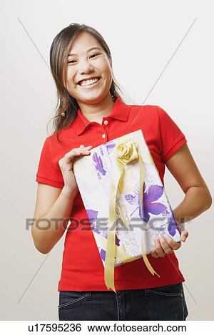 Stock Photograph - Portrait of a young woman holding a gift and looking cheerful. Fotosearch