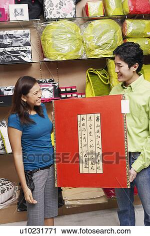 Young couple holding a painting and looking at each other in a store View Large Photo Image Stock Image - Young couple holding a painting and looking at each other in a store. Fotosearch