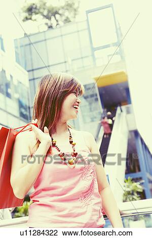 Stock Image - Young woman carrying a shopping bag and smiling. Fotosearch