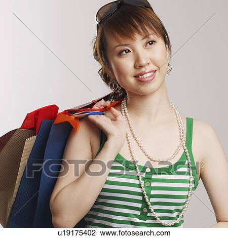 Stock Image - Close-up of a young woman carrying shopping bags and looking up. Fotosearch