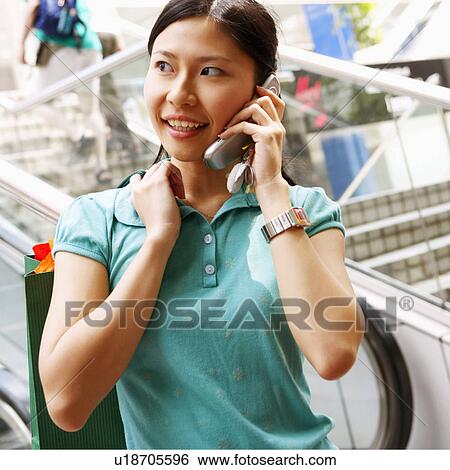 Stock Photograph - Close-up of a young woman talking on a mobile phone and carrying a shopping bag. Fotosearch