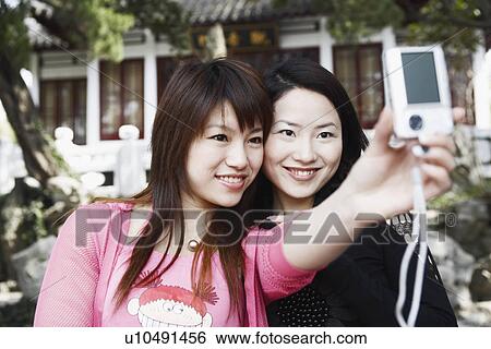 Stock Photograph - Close-up of two young women taking a photograph of themselves. Fotosearch