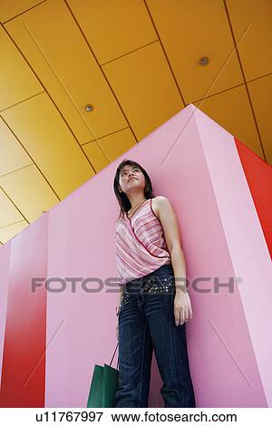 Stock Photo - Low angle view of a young woman holding a shopping bag. Fotosearch