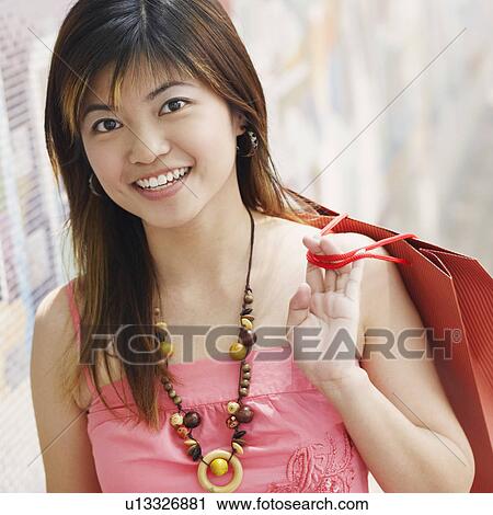 Portrait of a young woman carrying a shopping bag and smiling View Large Photo Image Stock Image - Portrait of a young woman carrying a shopping bag and smiling. Fotosearch