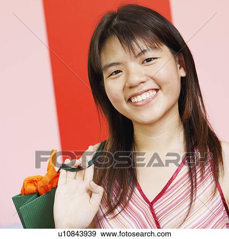 Portrait of a young woman carrying a shopping bag and smiling View Large Photo Image Stock Photo - Portrait of a young woman carrying a shopping bag and smiling. Fotosearch