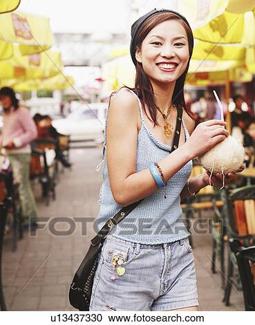 Stock Image - Portrait of a young woman holding a coconut drink. Fotosearch