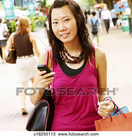 Stock Image - Portrait of a young woman holding a mobile phone and carrying shopping bags. Fotosearch