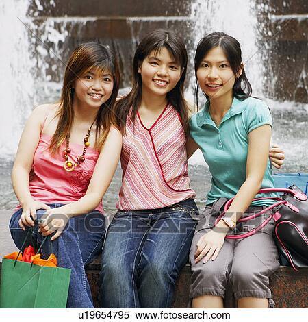 Stock Photography - Portrait of three young women sitting together at the edge of a fountain and posing. Fotosearch
