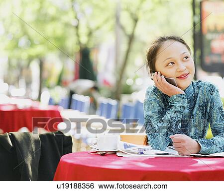 Young woman sitting in a restaurant and talking on a mobile phone View Large Photo Image Stock Photograph - Young woman sitting in a restaurant and talking on a mobile phone. Fotosearch