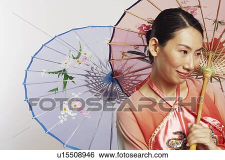 Stock Photograph - Close-up of a mid adult woman holding two umbrellas and smiling. Fotosearch