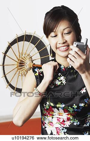 Close-up of a young woman holding a parasol looking at a mobile phone View Large Photo Image Stock Photograph - Close-up of a young woman holding a parasol looking at a mobile phone. Fotosearch