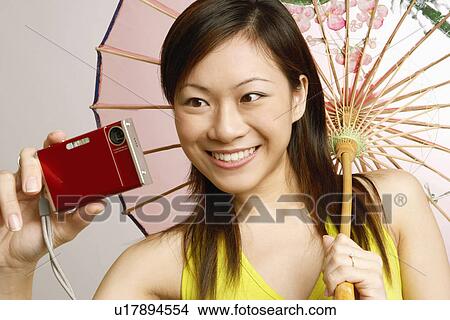 Close-up of a young woman taking a photograph of herself and holding a parasol View Large Photo Image Picture - Close-up of a young woman taking a photograph of herself and holding a parasol. Fotosearch