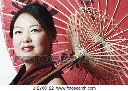 Stock Image - Portrait of a mid adult woman holding a parasol. Fotosearch