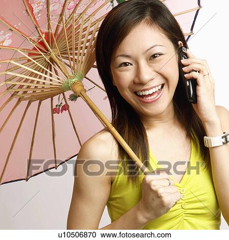 Stock Image - Portrait of a young woman holding a parasol and talking on a mobile phone. Fotosearch