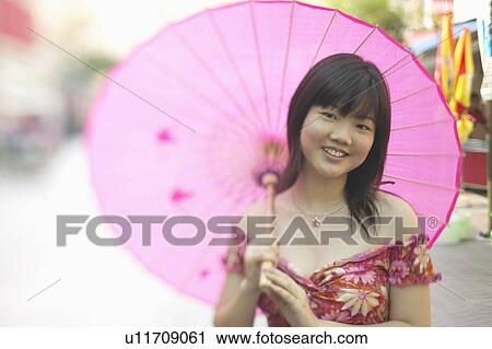 Stock Image - Portrait of a young woman holding a parasol smiling. Fotosearch
