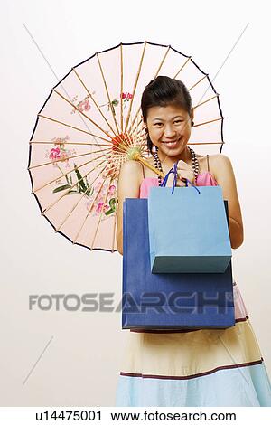 Stock Image - Portrait of a young woman holding a parasol and shopping bags. Fotosearch