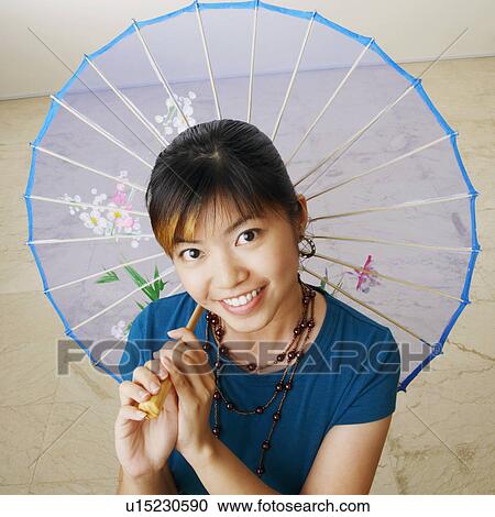 Stock Image - Portrait of a young woman holding a parasol and smiling. Fotosearch