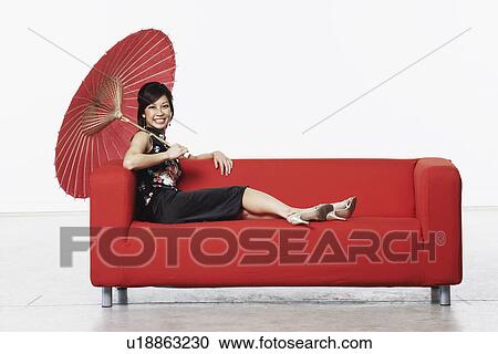 Portrait of a young woman sitting on a couch holding a parasol View Large Photo Image Stock Image - Portrait of a young woman sitting on a couch holding a parasol. Fotosearch