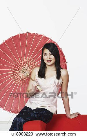 Portrait of a young woman sitting on a couch holding a parasol View Large Photo Image Stock Photo - Portrait of a young woman sitting on a couch holding a parasol. Fotosearch