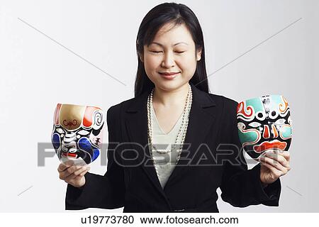 Stock Image - Close-up of a businesswoman holding two masks. Fotosearch