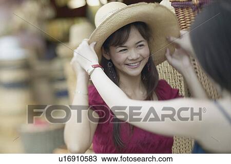 Stock Image - Close-up of a young woman trying on a straw hat. Fotosearch