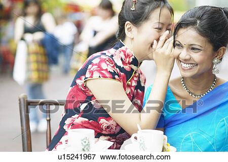 Close-up of a young woman whispering into another woman's ear View Large Photo Image Stock Photo - Close-up of a young woman whispering into another woman's ear. Fotosearch