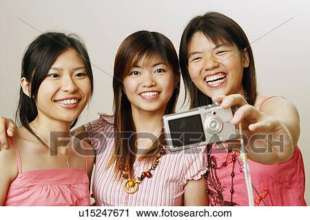 Stock Image - Close-up of three young women taking a picture of themselves. Fotosearch