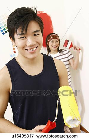 Stock Photo - Portrait of a young man holding a paint roller with a young woman standing in the background. Fotosearch