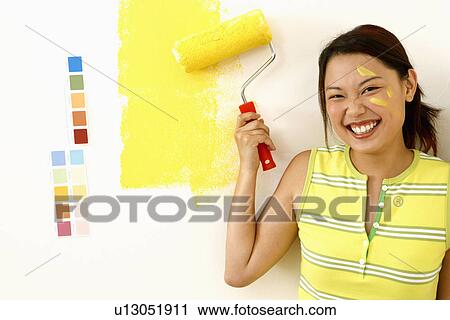 Stock Image - Portrait of a young woman holding a paint roller. Fotosearch
