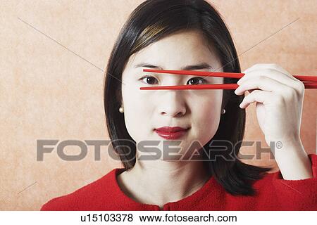 Stock Photo - Portrait of a young woman holding chopsticks in front of her face. Fotosearch