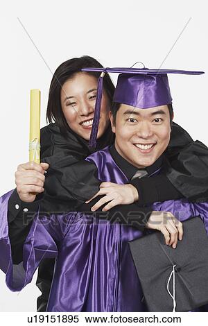 Stock Photography - Portrait of a young woman riding piggyback on a male graduate. Fotosearch
