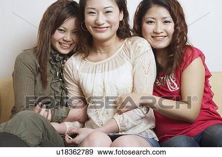 Stock Photo - Portrait of three young women sitting together smiling. Fotosearch