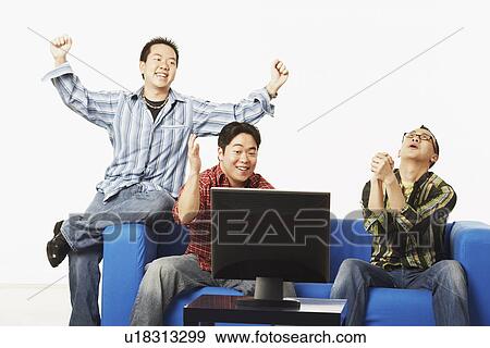 Three young men sitting on a couch in front of a flat screen monitor View Large Photo Image Stock Photo - Three young men sitting on a couch in front of a flat screen monitor. Fotosearch