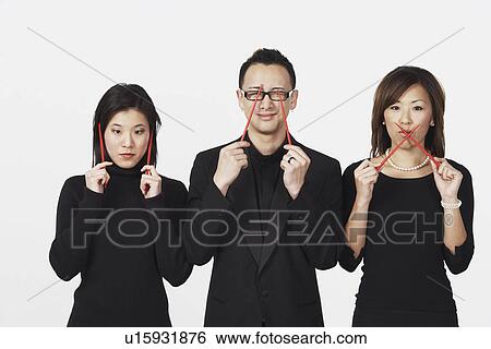 Stock Photograph - Two young women and a young man gesturing speak no evil, hear no evil, see no evil with chopsticks. Fotosearch